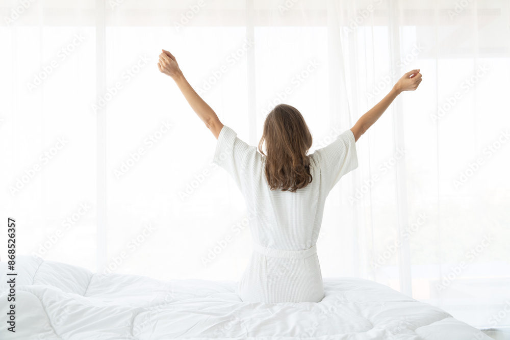 Woman stretching in bed after wake up. she sitting near the big white window while stretching on bed after waking up with sunrise at morning Woman stretching in bed after wake up. she sitting near the big white window while stretching on bed after waking up with sunrise at morning
