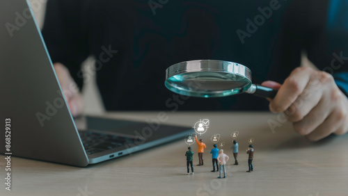 A close-up of a person's hand holding a magnifying glass over a group of miniature figures, individual. targeted search, recruitment, and selection processes in a professional or business context.