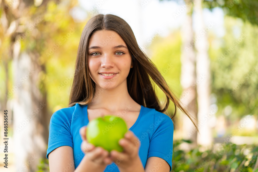 Teenager girl at outdoors holding an apple with happy expression Teenager girl at outdoors holding an apple with happy expression