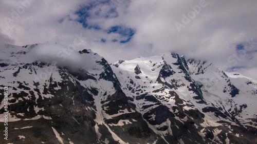 Felsiges schneebedecktes Alpenpanorama von Wolken umhüllt mit teilweise Blauem Himmel und weißen Wolken