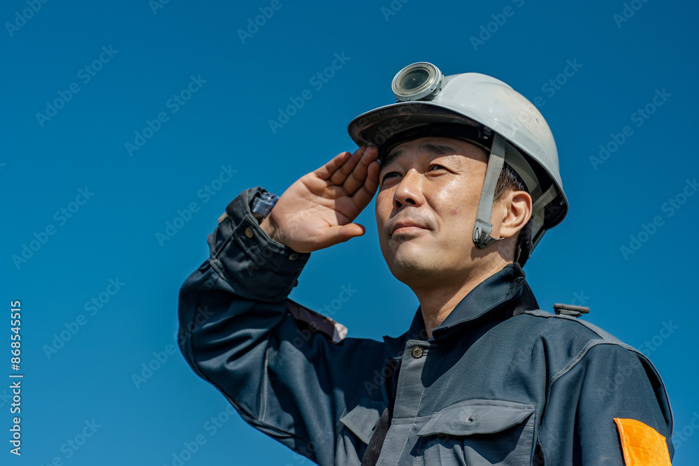 Smiling Japanese Engineer Saluting Under Blue Sky with Work Gear Smiling Japanese Engineer Saluting Under Blue Sky with Work Gear