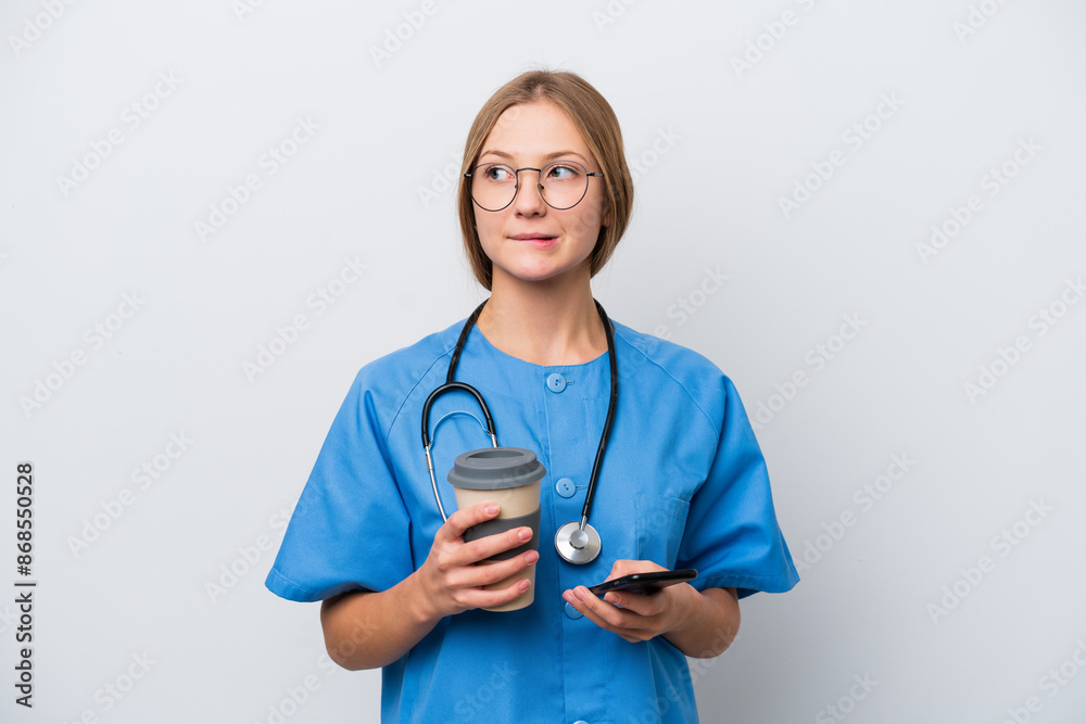 Young nurse doctor woman isolated on white background holding coffee to take away and a mobile while thinking something Young nurse doctor woman isolated on white background holding coffee to take away and a mobile while thinking something