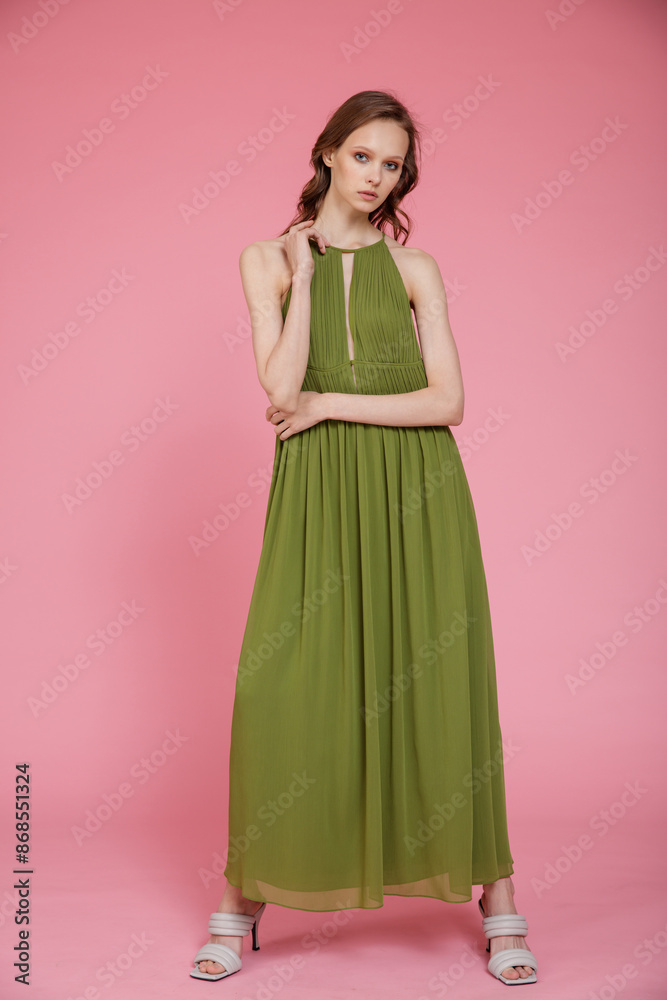 High fashion photo of a beautiful elegant young skinny woman in pretty long green dress posing on pink background. Slim figure. High fashion photo of a beautiful elegant young skinny woman in pretty long green dress posing on pink background. Slim figure.