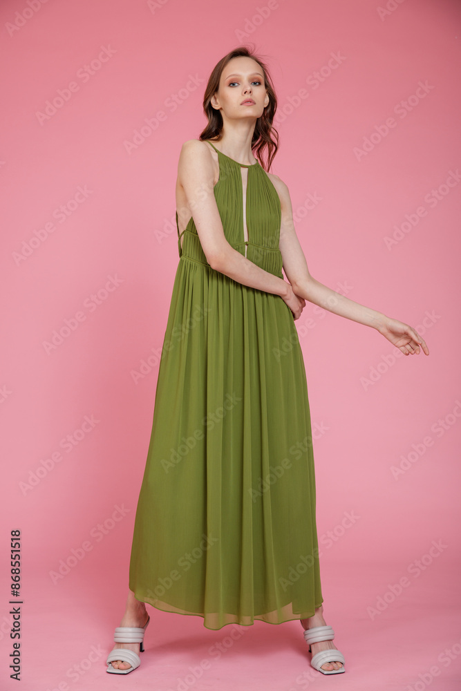 High fashion photo of a beautiful elegant young skinny woman in pretty long green dress posing on pink background. Slim figure. High fashion photo of a beautiful elegant young skinny woman in pretty long green dress posing on pink background. Slim figure.