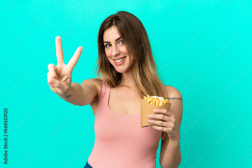 Caucasian woman holding fried chips isolated on blue background smiling and showing victory sign Caucasian woman holding fried chips isolated on blue background smiling and showing victory sign