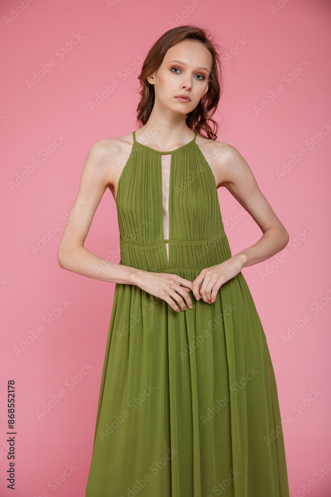 High fashion photo of a beautiful elegant young skinny woman in pretty long green dress posing on pink background. Slim figure. High fashion photo of a beautiful elegant young skinny woman in pretty long green dress posing on pink background. Slim figure.