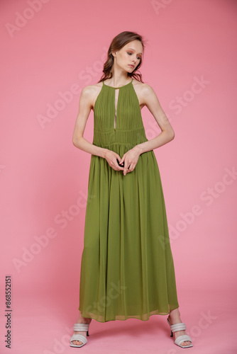 High fashion photo of a beautiful elegant young skinny woman in pretty long green dress posing on pink background. Slim figure.