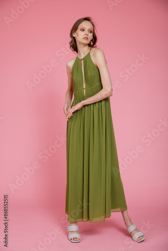 High fashion photo of a beautiful elegant young skinny woman in pretty long green dress posing on pink background. Slim figure.