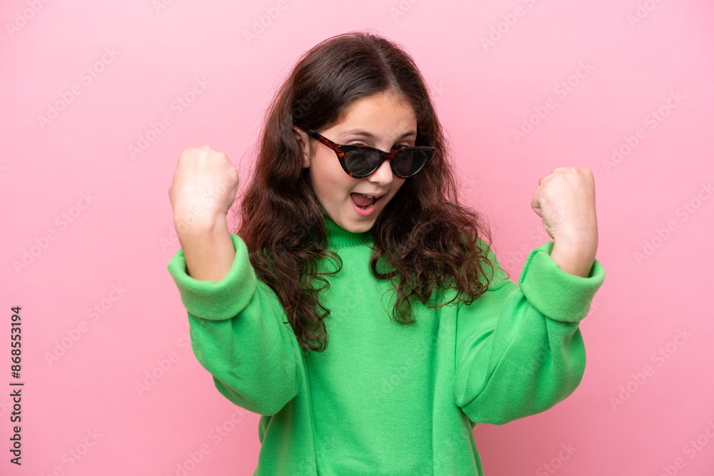 Little caucasian girl wearing sunglasses isolated on pink background celebrating a victory Little caucasian girl wearing sunglasses isolated on pink background celebrating a victory