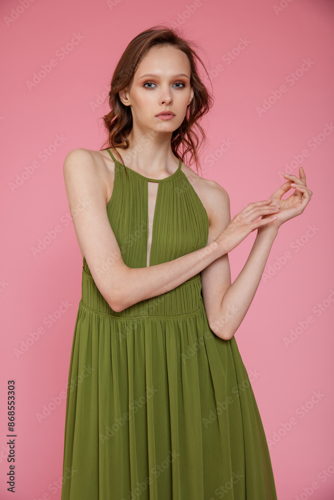 High fashion photo of a beautiful elegant young skinny woman in pretty long green dress posing on pink background. Slim figure. High fashion photo of a beautiful elegant young skinny woman in pretty long green dress posing on pink background. Slim figure.