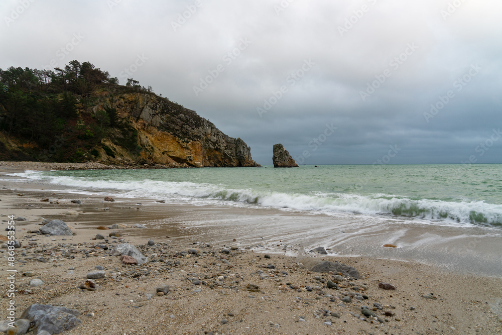 Sous un ciel couvert, la mer d'Iroise couleur émeraude, avec écume au pied des falaises et d'un îlot rocheux sur une plage de la presqu'île de Crozon en Bretagne. Sous un ciel couvert, la mer d'Iroise couleur émeraude, avec écume au pied des falaises et d'un îlot rocheux sur une plage de la presqu'île de Crozon en Bretagne.