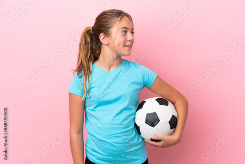 Little football player girl isolated on pink background looking side
