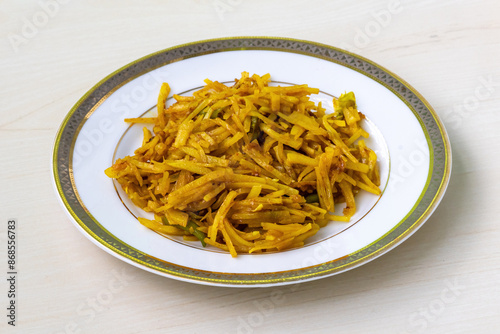 Delicious aloo bhaji or fried grated potato in a white plate on wooden background. Authentic bengali food which is thin potato slices deep fried using turmeric and some mild spices. photo