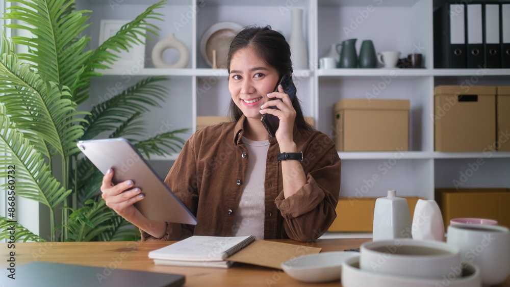 Successful small business owner talking by phone while working in craft pottery shop. Successful small business owner talking by phone while working in craft pottery shop.