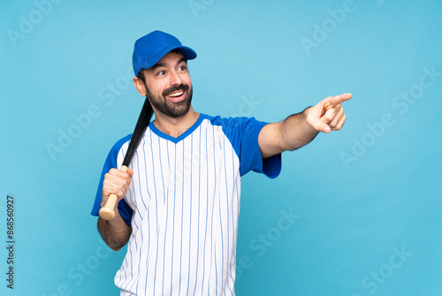 Photography Young man playing baseball over isolated blue background pointing away