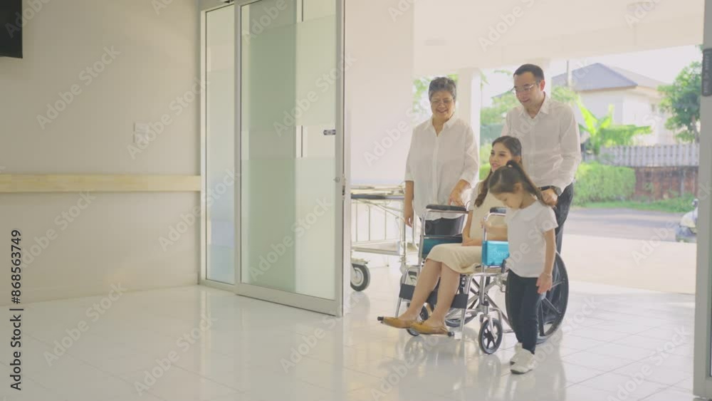 Asian family with grandmother, husband and pregnancy wife on wheelchair move pass through the gate to area near reception or counter in hospital and greeting by Caucasian nurse.