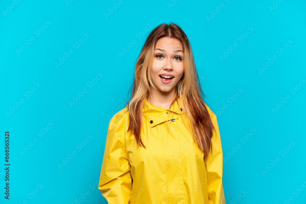 Teenager girl wearing a rainproof coat over isolated blue background with surprise facial expression