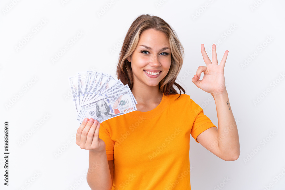 Young Russian girl holding dollars isolated on white background showing ok sign with fingers Young Russian girl holding dollars isolated on white background showing ok sign with fingers