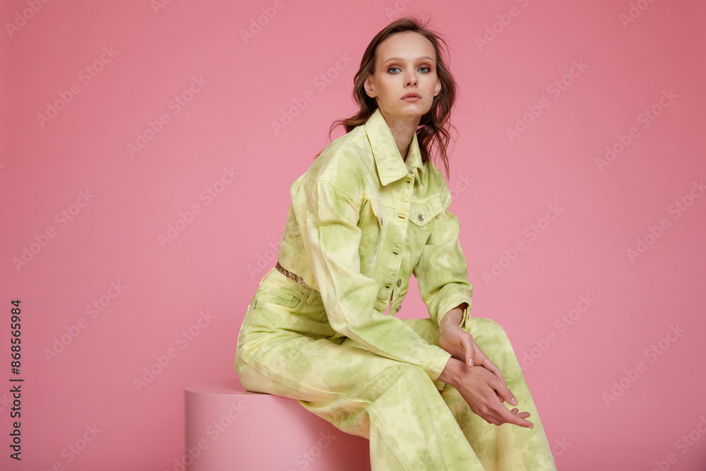 High fashion photo of a beautiful skinny young woman in pretty green military denim jeans pants, jacket, metallic bronze top posing on pink background. Slim figure. High fashion photo of a beautiful skinny young woman in pretty green military denim jeans pants, jacket, metallic bronze top posing on pink background. Slim figure.