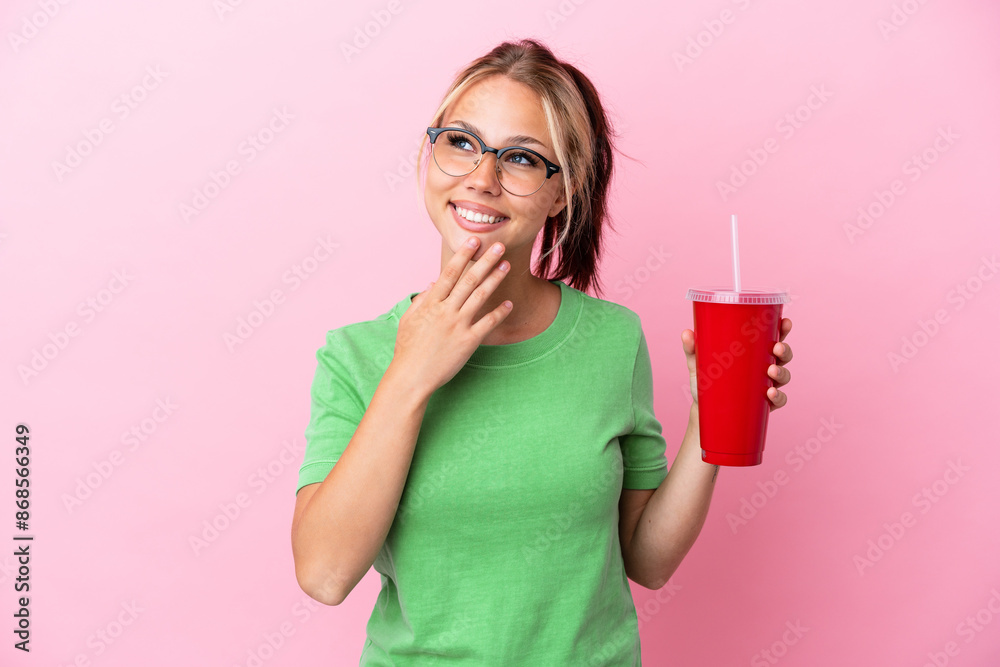 Young Russian woman holding a refreshment isolated on pink background looking up while smiling Young Russian woman holding a refreshment isolated on pink background looking up while smiling