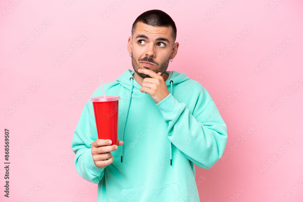 Young caucasian man holding soda isolated on pink background having doubts and thinking Young caucasian man holding soda isolated on pink background having doubts and thinking