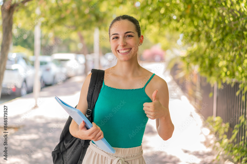 Naklejka premium Young pretty student woman at outdoors with thumbs up because something good has happened