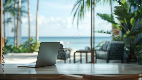 Tropical home office with ocean view. Laptop on a wooden desk with a blurred background of a tropical beach, perfect for travel and work-from-anywhere concepts. photo