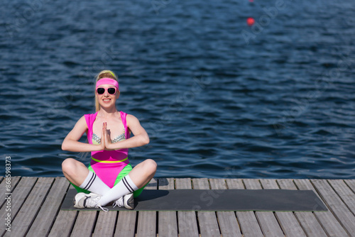 Young beautiful blonde woman in sports shorts, a pink bodysuit and pink sunglasses is doing sports outdoors. Doing exercises with dumbbells. Sports, Active lifestyle, sports training, healthy
