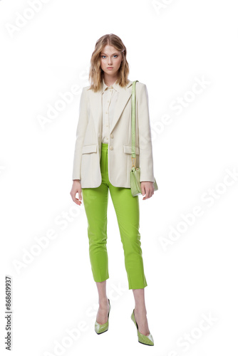 High fashion photo of a beautiful elegant young woman in pretty green pants, trousers, jacket, handbag posing on white background. Slim figure. Blonde