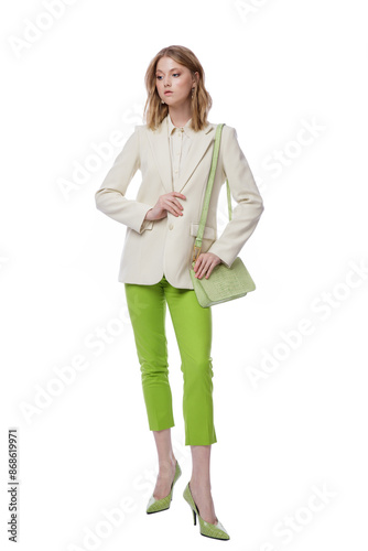 High fashion photo of a beautiful elegant young woman in pretty green pants, trousers, jacket, handbag posing on white background. Slim figure. Blonde