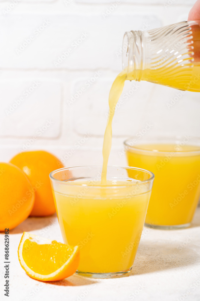 freshly squeezed orange juice is poured into a glass, vertical closeup freshly squeezed orange juice is poured into a glass, vertical closeup