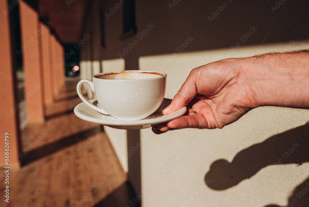 White cup of morning tasty coffee in the hand, sunny day