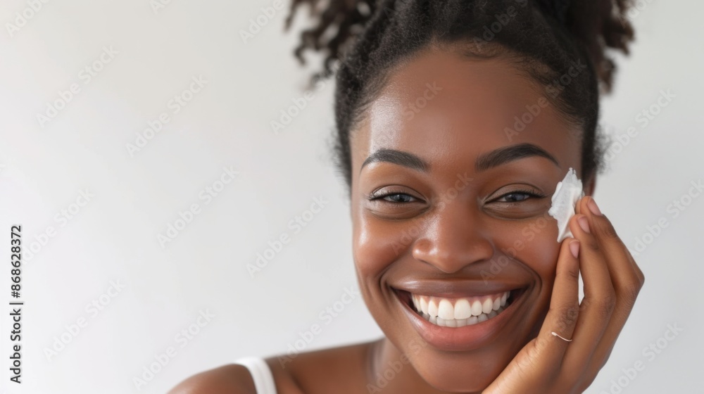 A woman is in a bright studio smiling as she applies skincare cream to her face A woman is in a bright studio smiling as she applies skincare cream to her face