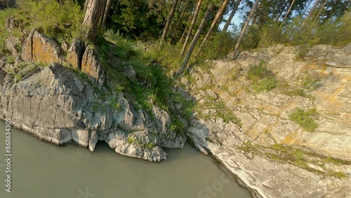 Shooting from a dynamic FPV drone. A flight over a bubbling mountain river with rapids. A flight over the forest and water. Beautiful young woman, standing on a rocky shore.