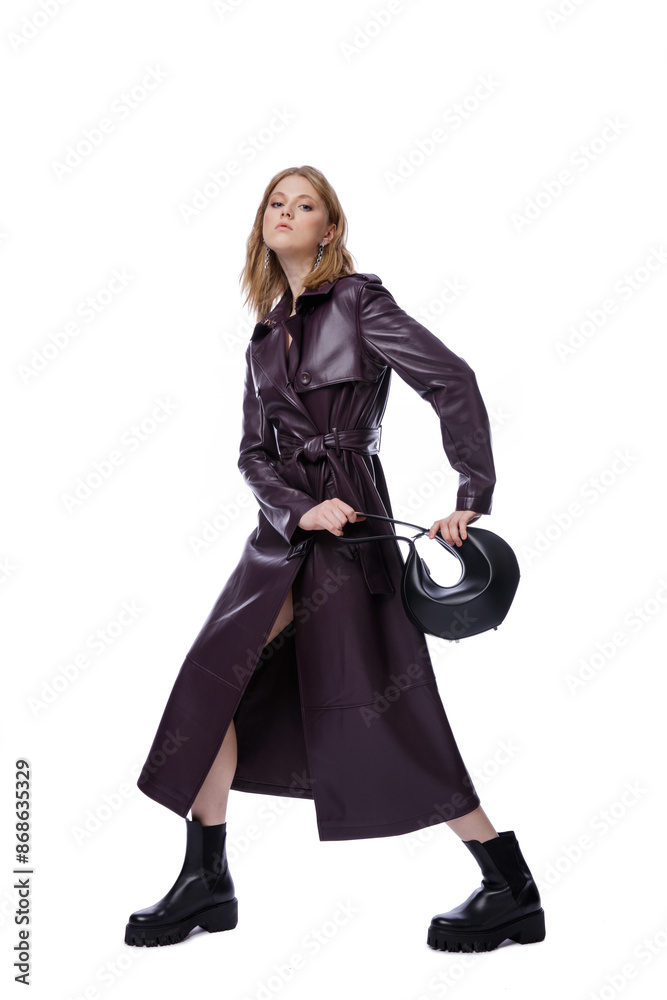 High fashion photo of a beautiful elegant young woman in pretty long purple lilac leather jacket, coat, handbag posing on white background. Slim figure. Blonde