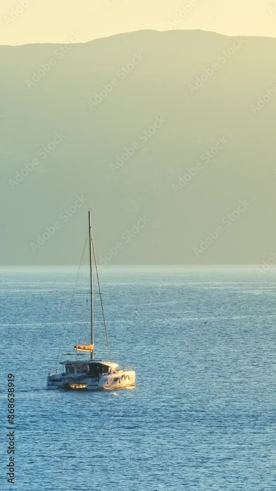 Sail boat at sunrise in Ionian sea, Greece. Sailing boat in the sea against the backdrop of mountains. Beautiful bay with sailing boat catamaran, Kefalonia island, Greece. Still shot Sail boat at sunrise in Ionian sea, Greece. Sailing boat in the sea against the backdrop of mountains. Beautiful bay with sailing boat catamaran, Kefalonia island, Greece. Still shot