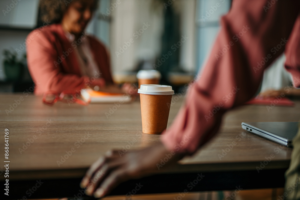 A coffee on the table while a businesswoman standing and running a meeting in the office. Coffee to go in a business concept A coffee on the table while a businesswoman standing and running a meeting in the office. Coffee to go in a business concept