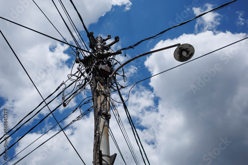 A busy utility pole with numerous wires and a streetlight against a blue sky