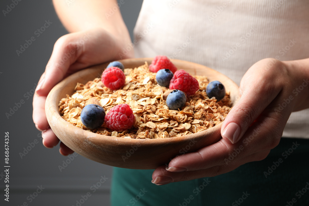 Woman holding bowl of tasty granola with berries and nuts on dark grey background, closeup Woman holding bowl of tasty granola with berries and nuts on dark grey background, closeup
