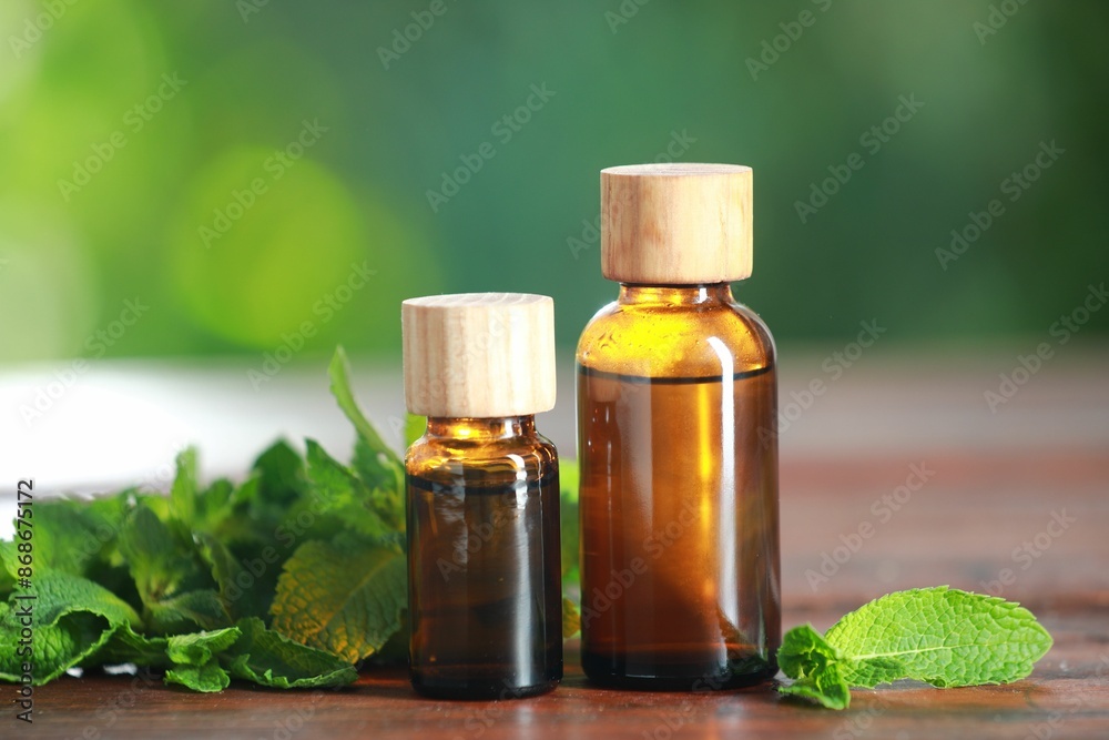 Bottles of mint essential oil and fresh leaves on wooden table Bottles of mint essential oil and fresh leaves on wooden table