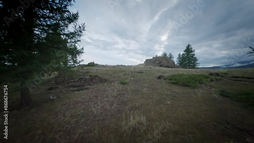 The FPV copter flies fast at low altitude over the hills. Cloudy evening weather in the mountainous area. Snowy mountains in background