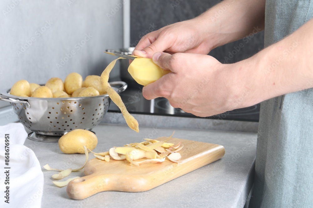 Man peeling fresh potato at grey countertop in kitchen, closeup Man peeling fresh potato at grey countertop in kitchen, closeup