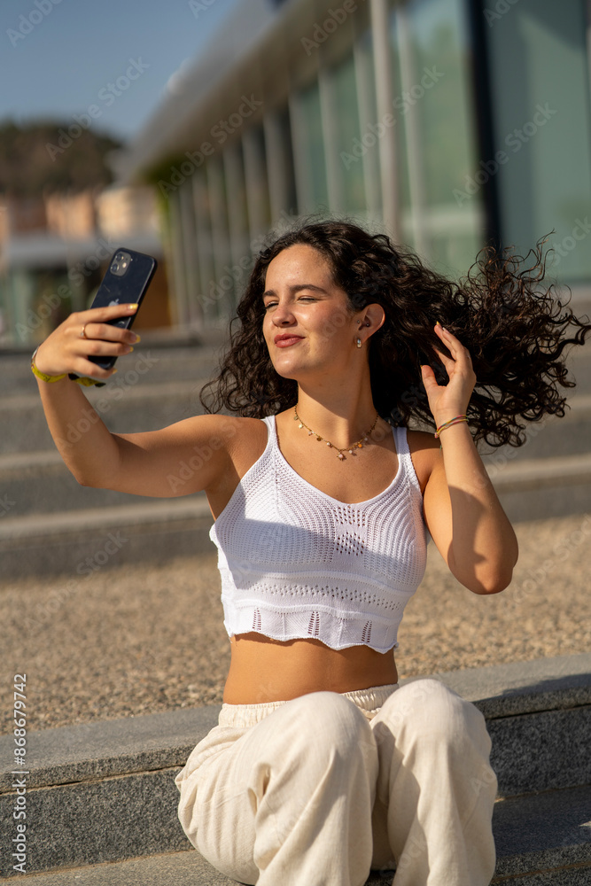 Chica joven en verano sonriendo haciendo fotos con el móvil en un lugar de mar y bonito. Pelo rizado y brillante. Chica joven en verano sonriendo haciendo fotos con el móvil en un lugar de mar y bonito. Pelo rizado y brillante.