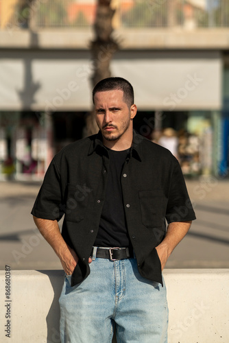 Chico joven modelo frente al mar y barco. Hombre con estilo informal. Ropa vaquera y negro.