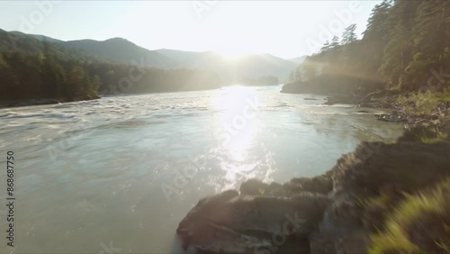 FPV drone flies over a turbulent mountain river at sunset. A flight past a young woman who admires the view. Aerial photography.