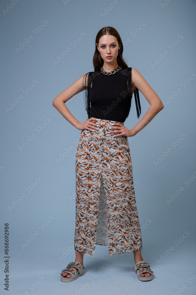 High fashion photo of a beautiful elegant young woman in pretty long skirt with floral pattern, black top posing on blue background. Slim figure. High fashion photo of a beautiful elegant young woman in pretty long skirt with floral pattern, black top posing on blue background. Slim figure.