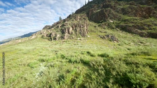 The FPV copter flies low to the trees. Hills covered with green trees, turbulent rivers, stone cliffs. Mountains in the background, cloudy weather, sunrise.