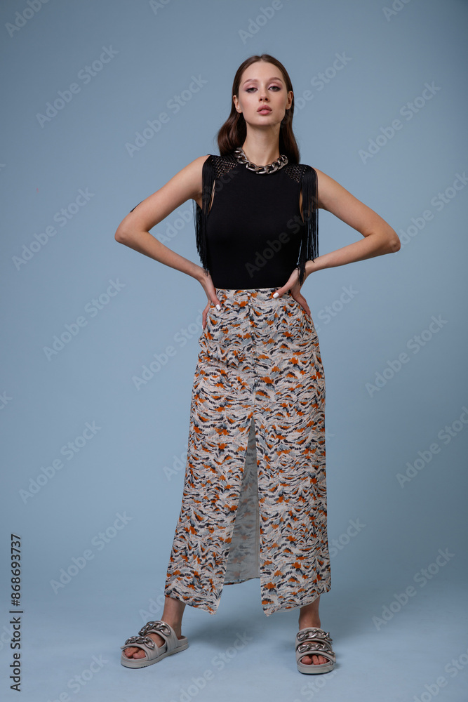 High fashion photo of a beautiful elegant young woman in pretty long skirt with floral pattern, black top posing on blue background. Slim figure. High fashion photo of a beautiful elegant young woman in pretty long skirt with floral pattern, black top posing on blue background. Slim figure.