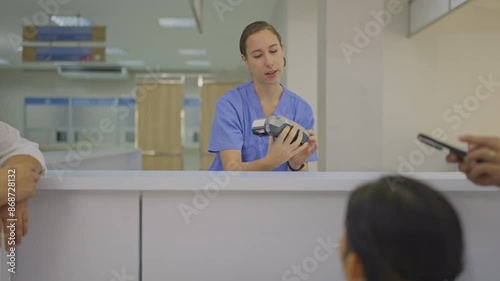 Side view of Asian man pay with mobile phone by scanning after register to hospital in the customer counter and take care by Caucasian nurse.