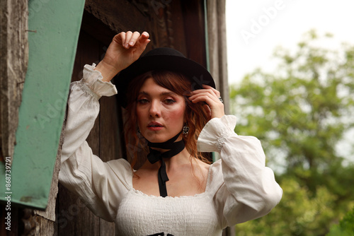 Beautiful woman in vintage dress and hat standing at old wooden door #868739791